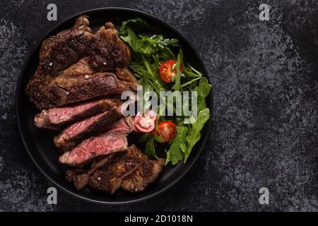 Steak de bœuf grillé aux épices sur une assiette noire, vue du dessus. Banque D'Images