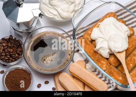 Tiramisu dessert cooking - cuisine italienne traditionnelle Savoiardi ladyfingers biscuits et crème dans un plat de cuisson en verre isolé sur blanc Banque D'Images