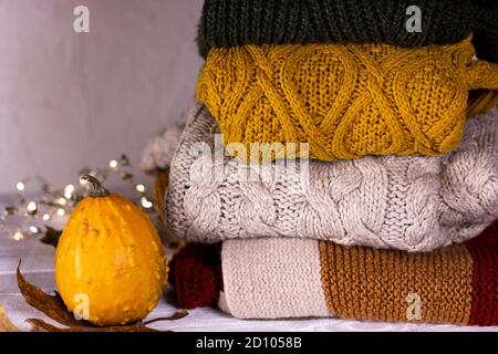 Automne. Citrouilles, feuilles de dray et chandails tricotés décorés de guirlandes de fées de Noël sur fond de bois blanc. Banque D'Images