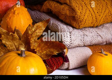 Automne. Citrouilles, feuilles de dray et chandails tricotés décorés de guirlandes de fées de Noël sur fond de bois blanc. Banque D'Images