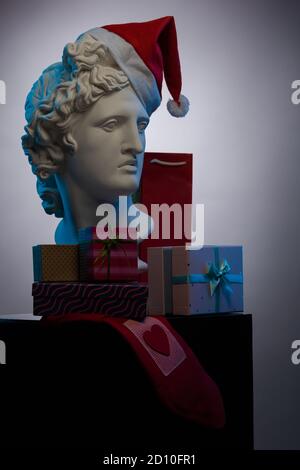 Buste d'Apollo Belvedere dans une casquette rouge du Père Noël, boîtes cadeaux et paquets, en lumière contour bleue sur fond multicolore. Composition pour CO Banque D'Images