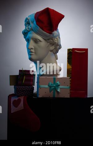 Buste d'Apollo Belvedere dans une casquette rouge du Père Noël, boîtes cadeaux et paquets, en lumière contour bleue sur fond multicolore. Composition pour CO Banque D'Images