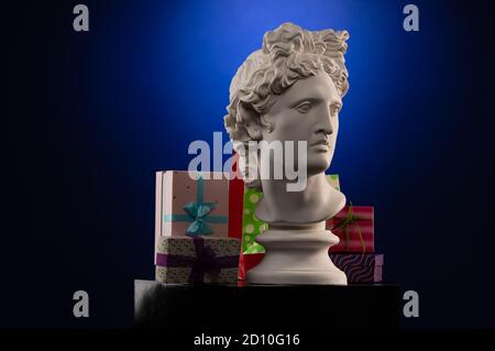 Statue en plâtre blanc d'Apollo Belvedere, boîtes à cadeaux et paquets, lumière bleue sur fond multicolore. Banque D'Images