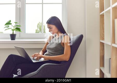 Femme asiatique employée de bureau assise dans un fauteuil et travaillant dessus ordinateur portable Banque D'Images