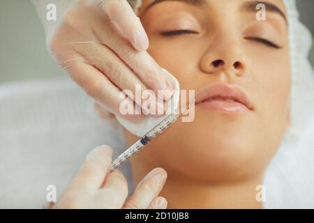 Les mains des thérapeutes injectent le botox de remplissage pour la correction de la lèvre supérieure de jeune femme Banque D'Images