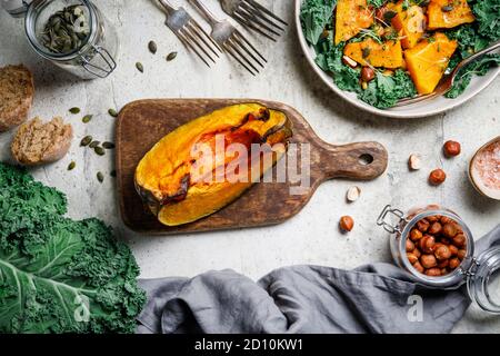 Citrouille rôtie sur une planche à découper en bois entourée de produits de saison d'automne. Kale, pain, noix et graines. Vue de dessus, arrière-plan du cadre alimentaire. Banque D'Images