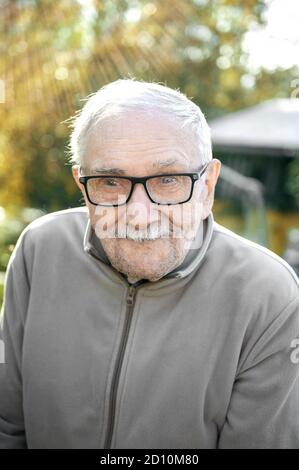 un vieil homme joyeux aux cheveux gris regarde l'interlocuteur et sourit. Le vieil homme ne peut pas très bien voir sans ses lunettes. Portrait d'un vieil homme joyeux Banque D'Images