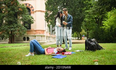 Une étudiante dormant sur l'herbe pendant que ses amis prennent photos d'elle Banque D'Images