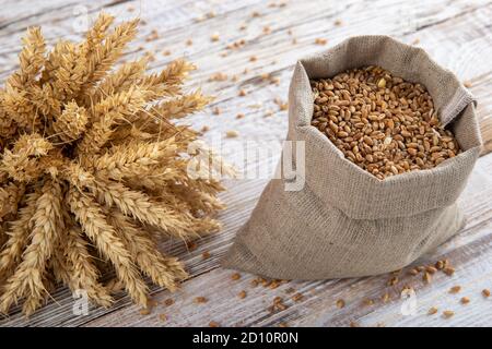 Sac de grains et d'oreilles de blé sur fond de bois. Produits naturels pour la fabrication de farine pour le pain et autres produits de boulangerie. Banque D'Images