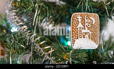 Pain d'épice sucré et corde argentée sur les aiguilles d'un arbre de Noël artificiel orné. Gros plan d'un biscuit traditionnel de Noël suspendu sur une branche verte. Banque D'Images
