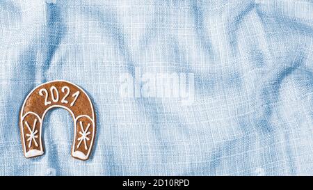 Jeu de fers à cheval pour 2021 Happy Year sur fond textile bleu. Biscuit au pain d'épice au four très orné pour avoir de la chance en forme de chaussure de cheval sur un tissu ondulé. Banque D'Images