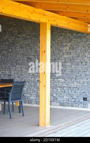 Colonne en bois de la terrasse extérieure. Carrelage en bois et en céramique. Mur recouvert de pierre avec prise visible. Partie de la table et de la chaise de dinnig visible. Banque D'Images