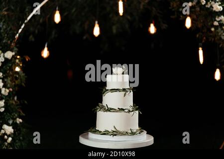 Gâteau de mariage minimaliste à trois niveaux à l'arrière-plan des lumières. Gâteau au mariage Banque D'Images