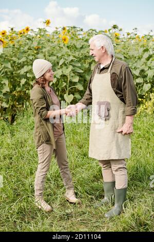 Joyeux agriculteur de sexe masculin en vêtements de travail en lui serrant la main collègue de femme mature Banque D'Images