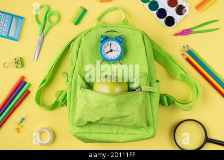 Se préparer pour le concept d'école. Haut au-dessus de la vue de la tête photo du réveil bleu pomme vert sac à dos coloré papeterie isolée sur le dos jaune Banque D'Images
