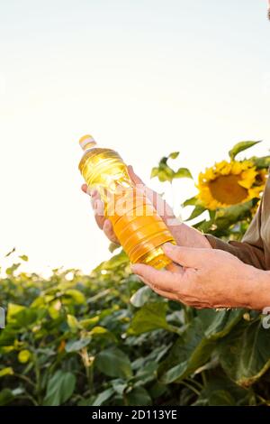 Mains d'un agriculteur contemporain senior tenant une bouteille d'huile de tournesol Banque D'Images