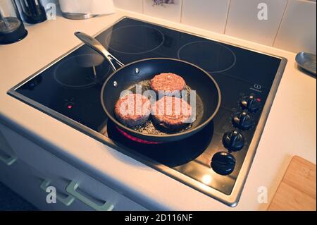 Angle latéral de trois beefburgers cuisant dans une poêle sur une plaque de cuisson Banque D'Images