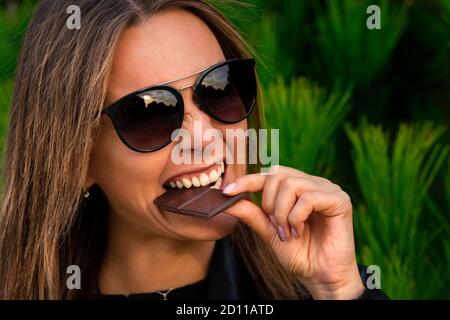 Jolie jeune femme fatiguée de stress et très heureuse de manger de la barre de chocolat. Gros plan de la femme visage piquant du chocolat noir. Banque D'Images