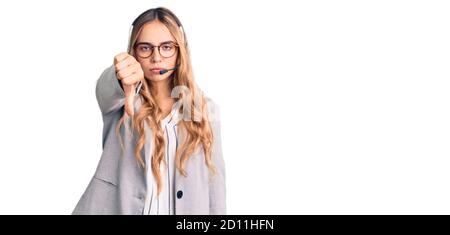 Jeune belle femme blonde portant le casque d'agent de centre d'appel, aspect malheureux et fâché montrant le rejet et négatif avec les pouces vers le bas geste. Mauvais Banque D'Images