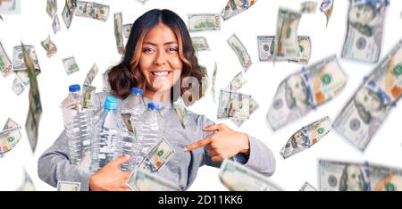 Jeune belle femme de race mixte tenant des bouteilles en plastique de recyclage souriant contenchez-vous de pointer avec votre main et votre doigt Banque D'Images