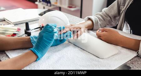 Manucure moderne dans le coronavirus épidémique. Femme afro-américaine en gants de caoutchouc couvre les ongles du client sur la table avec l'équipement et les bouteilles de poli Banque D'Images