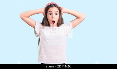 Mignon hispanique enfant fille portant décontracté blanc tshirt fou et peur avec les mains sur la tête, peur et surpris de choc avec la bouche ouverte Banque D'Images