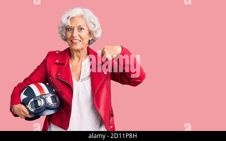 Femme sénior à cheveux gris tenant un casque de moto pointant du doigt vers un vous sourire heureux et fier Banque D'Images