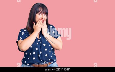 Jeune femme de taille plus portant des vêtements décontractés riant et Giggle embarrassé couvrant la bouche avec les mains, les potins et le concept de scandale Banque D'Images