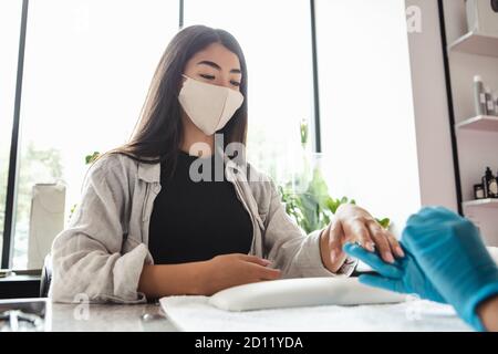 Ouverture du studio de beauté après verrouillage. Femme asiatique cliente dans le masque de protection regarde maître dans les gants de caoutchouc, faisant la manucure Banque D'Images