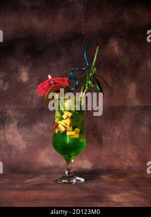 Un verre de jus à base de kiwi avec glace, morceaux de fruits, parapluie et pailles. Gros plan. Banque D'Images