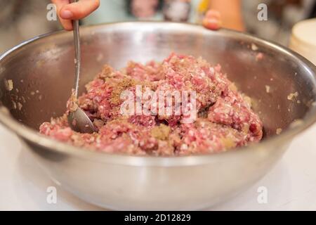 remuer la viande hachée à la main dans un bol métallique après ajouter le poivre Banque D'Images