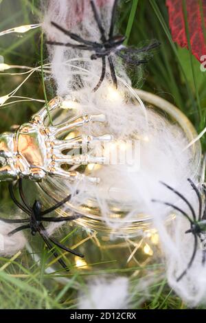 toile d'araignée et araignées dans un pot en verre avec guirlande et main de squelette sur l'herbe verte. halloween holiday concept Banque D'Images