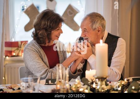 Heureux couple senior à l'intérieur à la maison assis à la table à Noël, parlant. Banque D'Images
