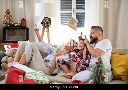 Famille avec petite fille à l'intérieur à la maison à Noël, ayant la vidéoconférence. Banque D'Images