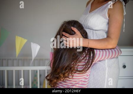 Portrait d'une femme enceinte avec une petite fille à l'intérieur à la maison, embrassant. Banque D'Images