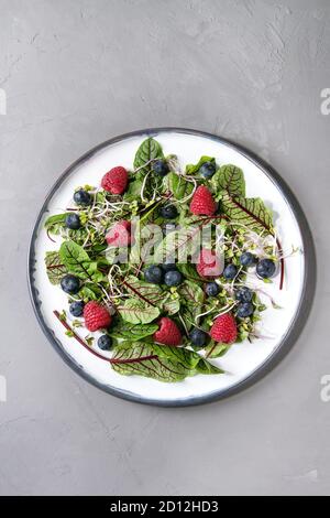 Salade verte aux fruits rouges vegan fraise, bleuet, jeunes pousses, feuilles de betterave sur une plaque en céramique sur fond de béton gris. Vue de dessus, de l'espace. Banque D'Images