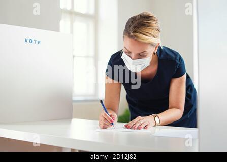 Portrait d'une femme votant avec masque facial dans le lieu de vote, élections et concept du coronavirus. Banque D'Images