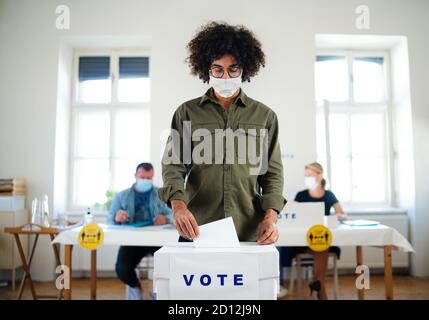 Jeune homme mettant son vote dans les urnes, les élections et le coronavirus. Banque D'Images