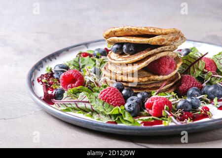 Pois chiches vegan pancakes servis en assiette avec une salade verte les jeunes feuilles, les pousses de betterave, des petits fruits, sauce aux baies plus gray table de cuisine. Close up. Healt Banque D'Images