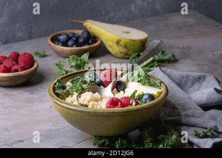 Porridge au quinoa vegan with kale, fraises, bleuets, de tranches de poire, de miel sur le balancier dans Bol en céramique avec des ingrédients ci-dessus et plus de serviette en tissu Banque D'Images