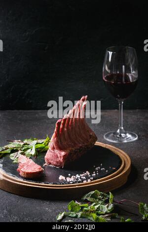 Carré d'agneau en tranches grillées avec du yogourt sauce à la menthe servie avec une salade verte les jeunes feuilles de betterave, verre de vin rouge, sel rose sur ardoise en bois ronde b Banque D'Images