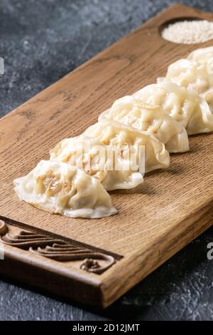 Les Gyozas raviolis asiatiques potstickers servi avec du sésame sur planche en bois de style asiatique sur fond de texture noire. Close up. Banque D'Images