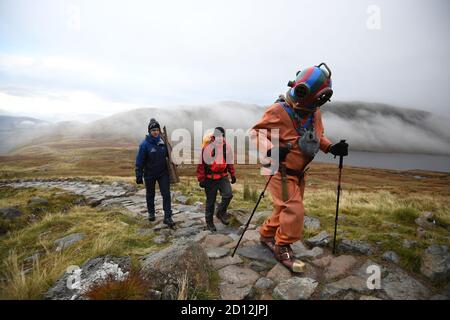 Lloyd Scott, collecteur de fonds vétéran, qui tente de grimper les trois sommets tout en portant un costume de plongée en haute mer, est suivi par des membres de son équipe de soutien lors de son défi sur Ben Nevis en Écosse. Banque D'Images