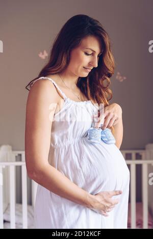 La femme enceinte porte une paire de chaussures pour bébé Banque D'Images