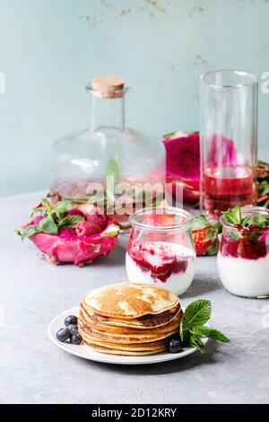 Pile de crêpes maison servi sur une assiette de fruits rouges, menthe, pots de verre de yaourt, une bouteille de limonade, salade de fruits en rose fruit du dragon gris sur te Banque D'Images