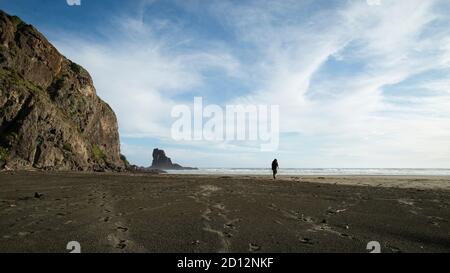 Marcher sur la plage de sable noir Anawhata avec le rocher Keyhole au loin, Waitakere, Auckland Banque D'Images