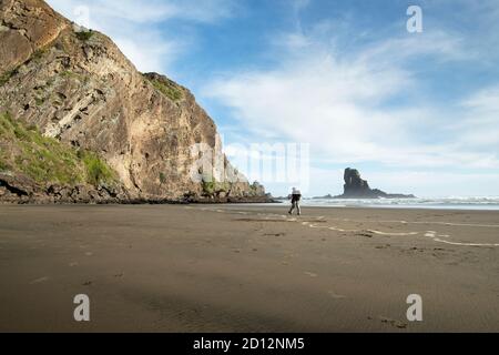 Marcher sur la plage de sable noir Anawhata avec le rocher Keyhole au loin, Waitakere, Auckland Banque D'Images