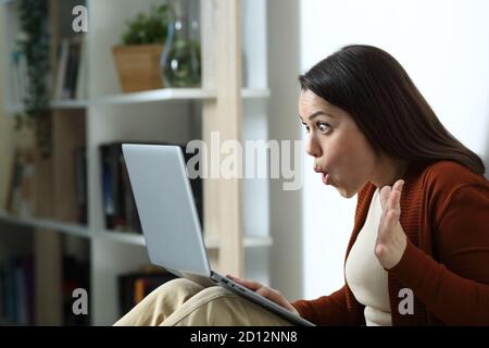 Une femme surprise vérifie un ordinateur portable assis sur le sol du nuit à la maison Banque D'Images