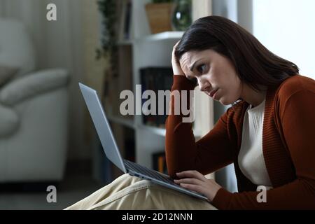 Triste femme vérifiant les mauvaises nouvelles sur ordinateur portable à la maison dans la nuit Banque D'Images