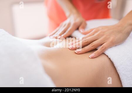 Une femme se fait masser le ventre dans une salle de procédure lumineuse. Massage anti-cellulite, diastase. Banque D'Images